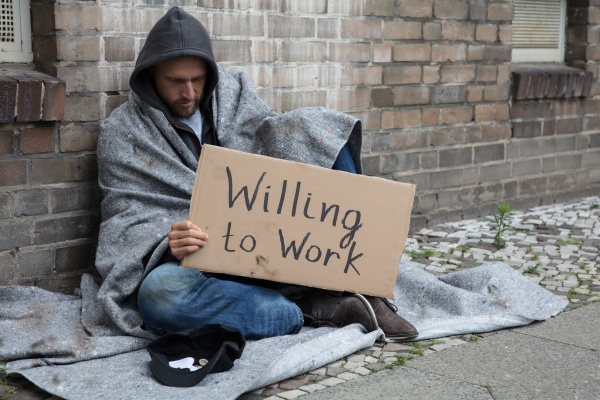 obdachloser mann haelt karton mit text