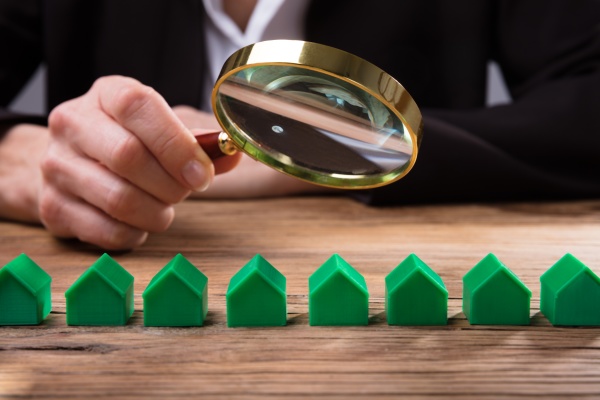 businessperson holding magnifying glass over house