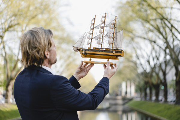 geschaeftsmann haelt modellschiff an einem kanal