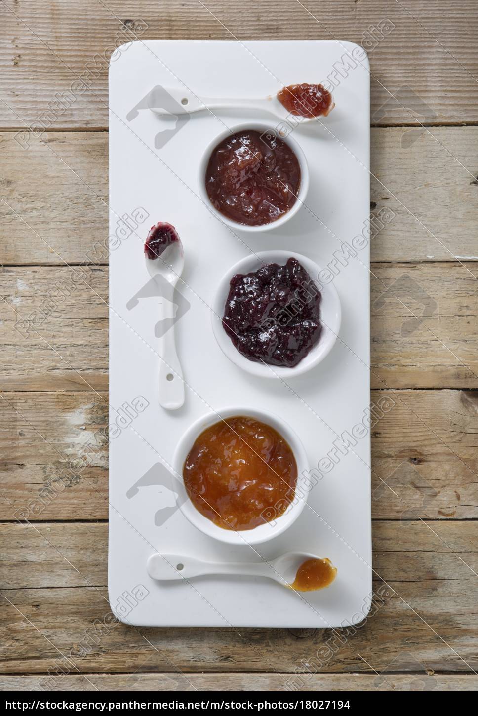 Three types of jam in bowls with spoons on a board Stock Photo