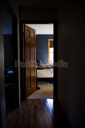 Girl Carrying Baby Sitting On Bed Seen From Doorway At